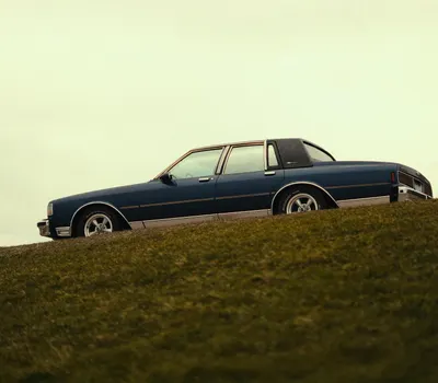 Classic 1980s Chevrolet car parked on a grassy hill, showcasing vintage automoti 4k aesthetic wallpaper