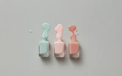 Pastel nail polish bottles with vibrant spills on a gray background. 4k aesthetic wallpaper