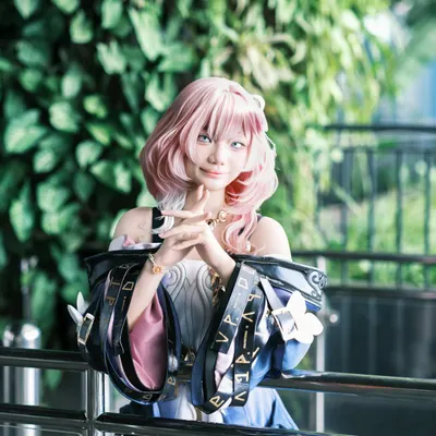 A pink-haired cosplayer posing against a vibrant green backdrop indoors. 4k anime wallpaper