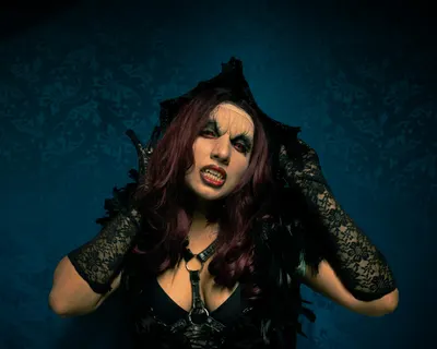 A woman in gothic attire poses against a patterned wall with bold makeup and lac 4k dark wallpaper