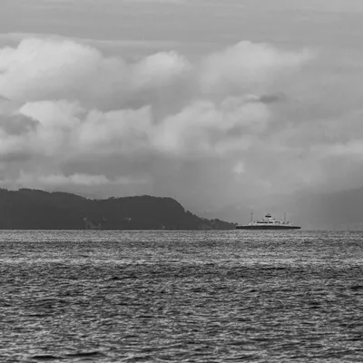 Dramatic black and white seascape with a solitary ship, cloudy sky, and distant  4k dark wallpaper