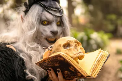 A mystical character holding a skull and spellbook in a forest setting. 4k fantasy wallpaper