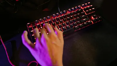 A hand engaging with a glowing mechanical gaming keyboard in a dark setting. 4k gaming wallpaper
