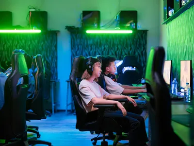 Teenagers immersed in online gaming in a neon-lit room, showcasing modern techno 4k gaming wallpaper