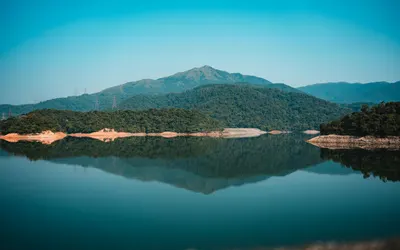 Calm lake with mountains and green forests reflected under a blue sky in serene  4k lake wallpaper