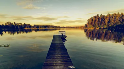 Serene landscape of a wooden jetty over a calm lake at sunset, reflecting trees  4k lake wallpaper