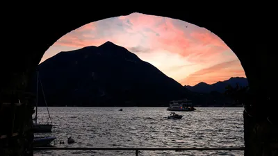 Tranquil sunset over Lake Como with boats and mountains in Varenna, Italy. 4k lake wallpaper