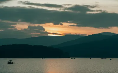 Tranquil sunset scene over a mountain lake with silhouettes of boats. 4k lake wallpaper