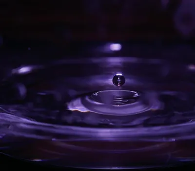 A mesmerizing close-up of a water droplet creating ripples with a purple tint, s 4k macro wallpaper
