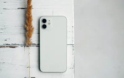 A white smartphone alongside dry grass on a rustic white wooden table, showcasin 4k minimal wallpaper