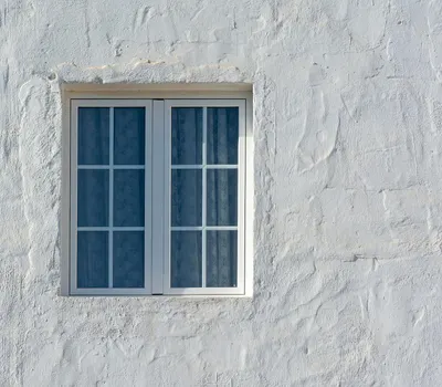 A whitewashed wall featuring a rustic window, captured in natural light. 4k minimal wallpaper