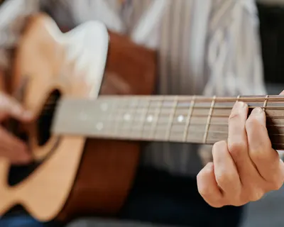 A person strumming chords on an acoustic guitar, focusing on fretboard technique 4k music wallpaper