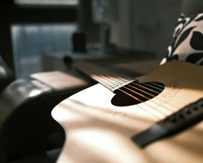 Artistic close-up shot of an acoustic guitar bathed in soft, warm light indoors. 4k music wallpaper