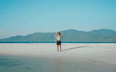 Young man enjoying a sunny day on a serene tropical beach with mountain views. 4k nature wallpaper