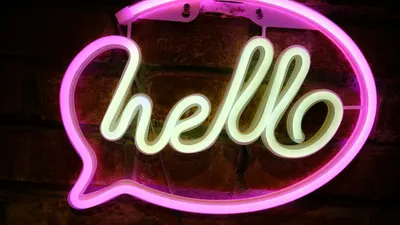 Vibrant pink neon 'Hello' sign casting light against a brick wall. 4k neon wallpaper