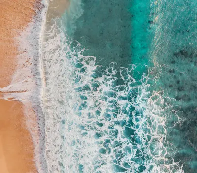 A mesmerizing aerial view of waves crashing onto a sandy tropical beach. 4k ocean wallpaper