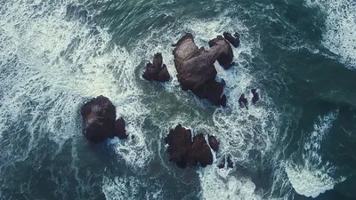 Dynamic aerial view of ocean waves crashing against rocky structures, captured f 4k ocean wallpaper