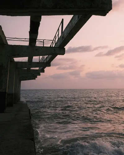 A tranquil view of a pier extending into the ocean under a serene sunset sky, pe 4k sunset wallpaper