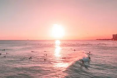 A vibrant sunset scene with surfers riding waves on a summer beach. 4k sunset wallpaper